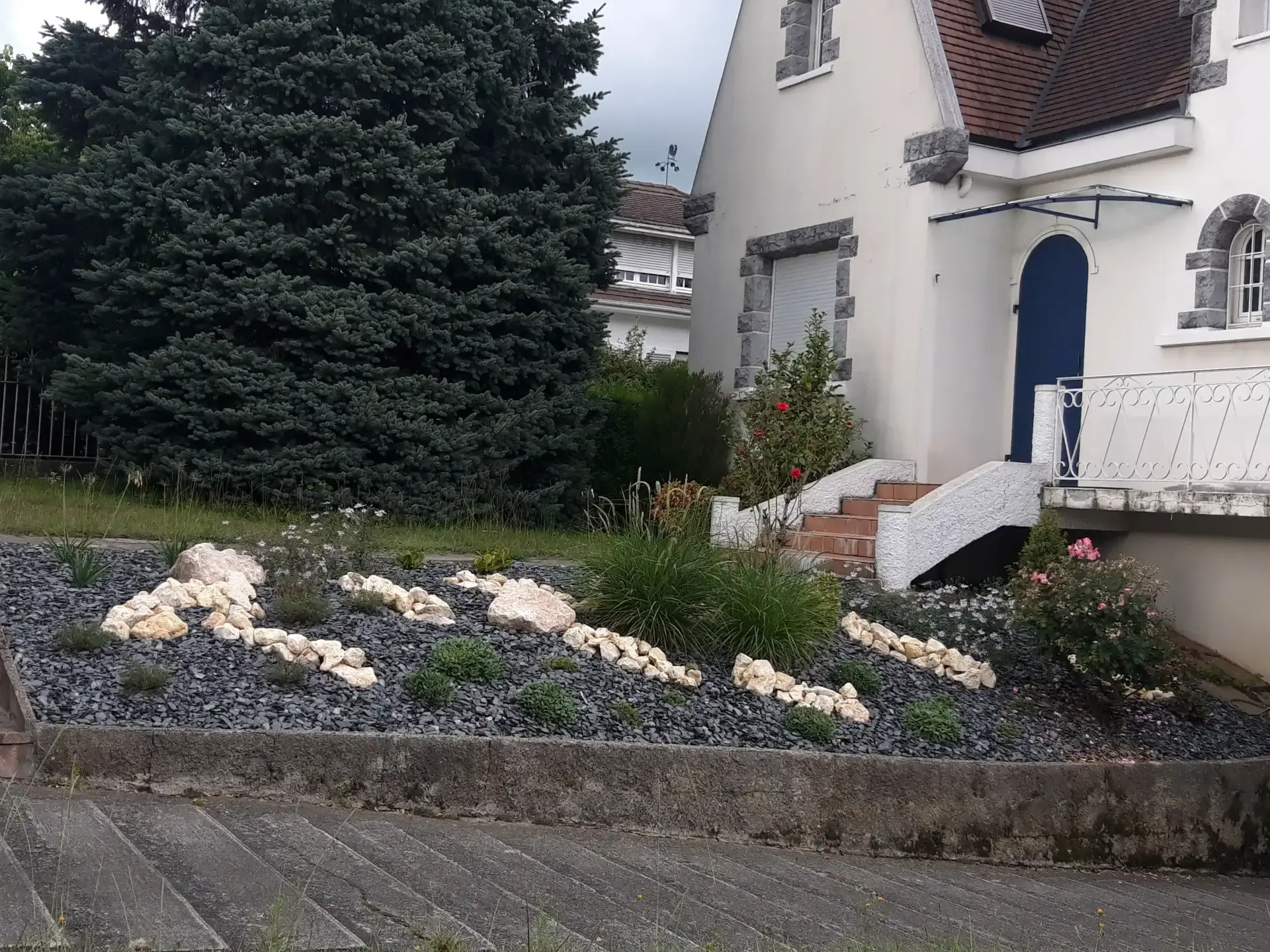Aménagement minéral devant une maison avec ardoise, pierres claires et plantations