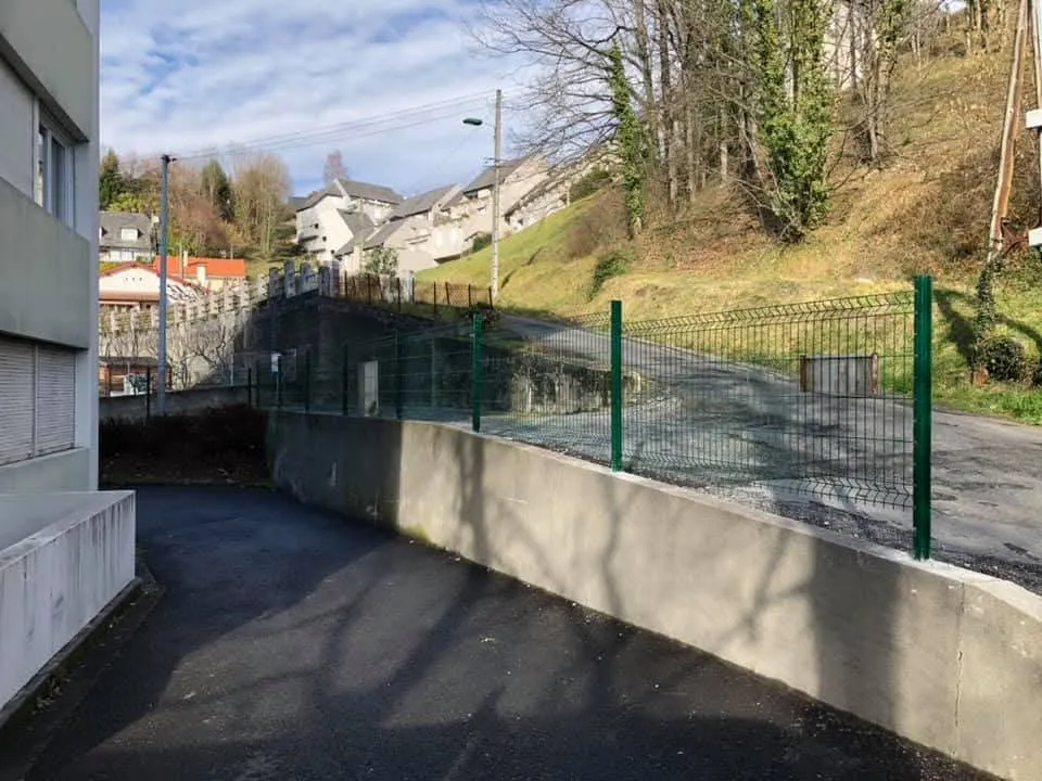 Clôture grillagée verte posée sur un muret dans un environnement arboré
