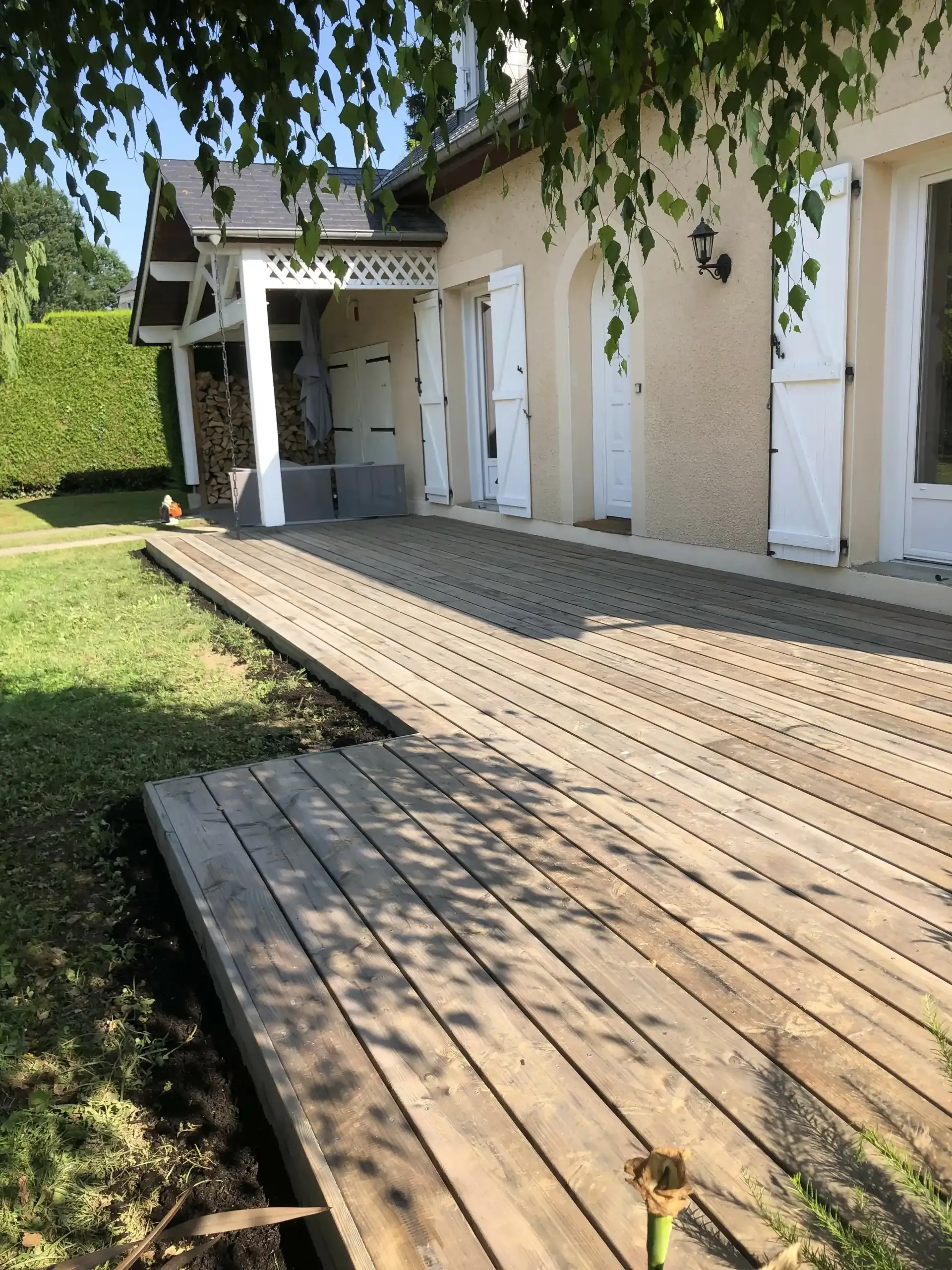 Grande terrasse en lames de bois aménagée au pied d’une maison et bordée de pelouse